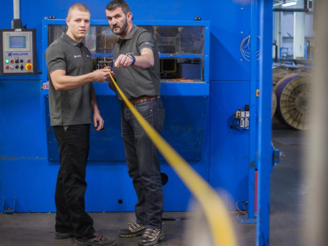 Zwei Techniker prüfen ein längliches, helles Mikroduct oder Kabel in Emtelle‑Produktionsabteilung