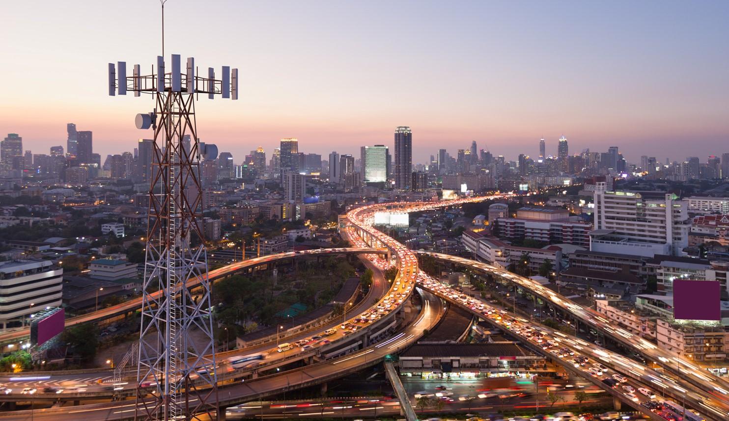 Luftaufnahme einer Großstadt mit Hochhäusern und Stadtautobahnen. Im Vordergrund ist eine große Antenne zu sehen mit verschiedenen Sendern.