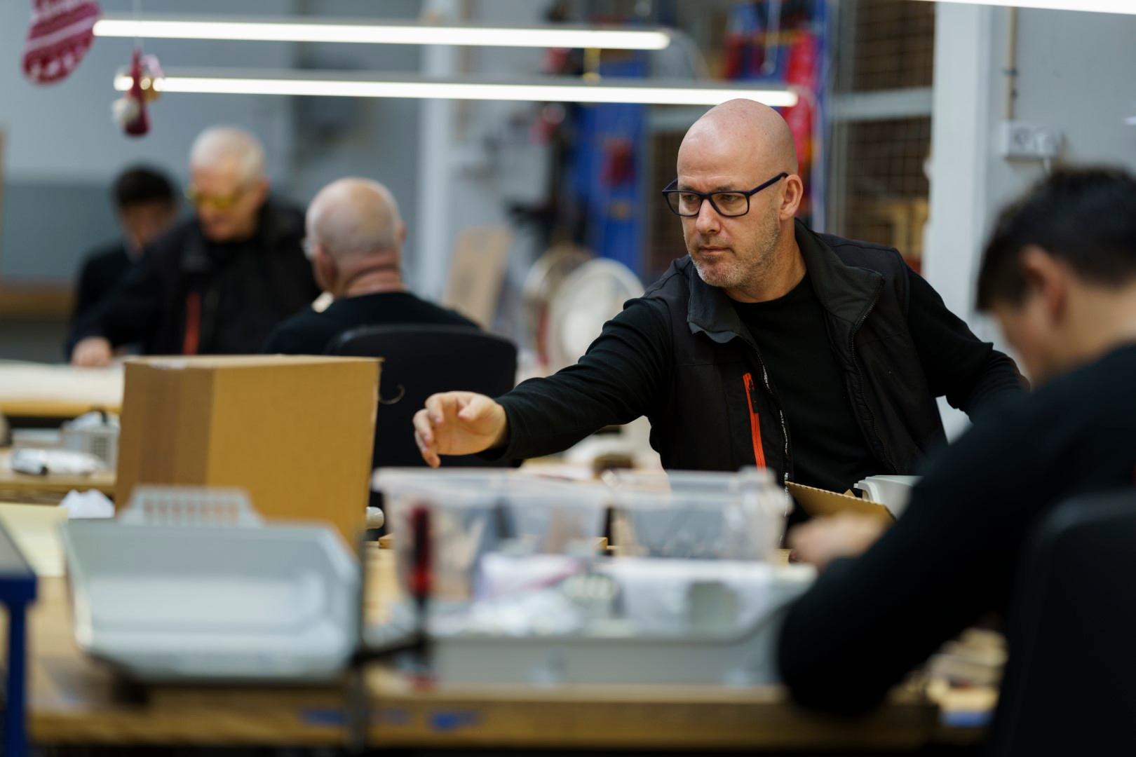 Mehrere Produktionsmitarbeiter die an Ihren Arbeitstischen Glasfaser Spleißboxen konfektionieren.